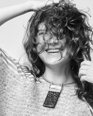 Student Nadja Cabana wears a short necklace with a silver ceramic pendant over a knitted sweater, she laughs heartily