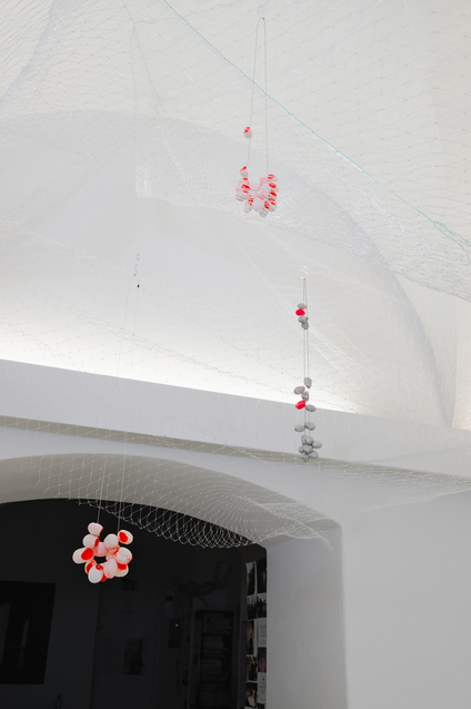 In the exhibition Mulberry Tubes, jewellery artist Michaela Rapp presents coloured cocoon necklaces from the IMAGO collection inside a see-through net hanging down from the ceiling as if they were floating.