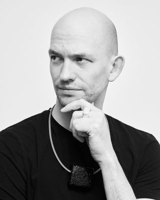 Young man wears a short necklace with a silver ceramic pendant over a black T-shirt, his look is serious