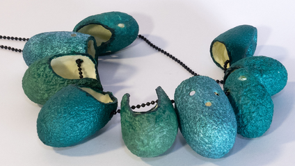 Necklace with 9 threaded silk cocoons open at the front, painted in emerald green on the outside and night luminescent pigment on the inside