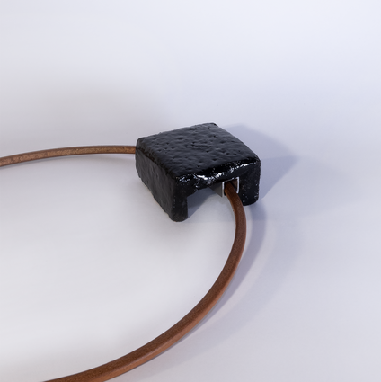 Pendant made of a square black glazed ceramic piece on a heavy reddish leather strap