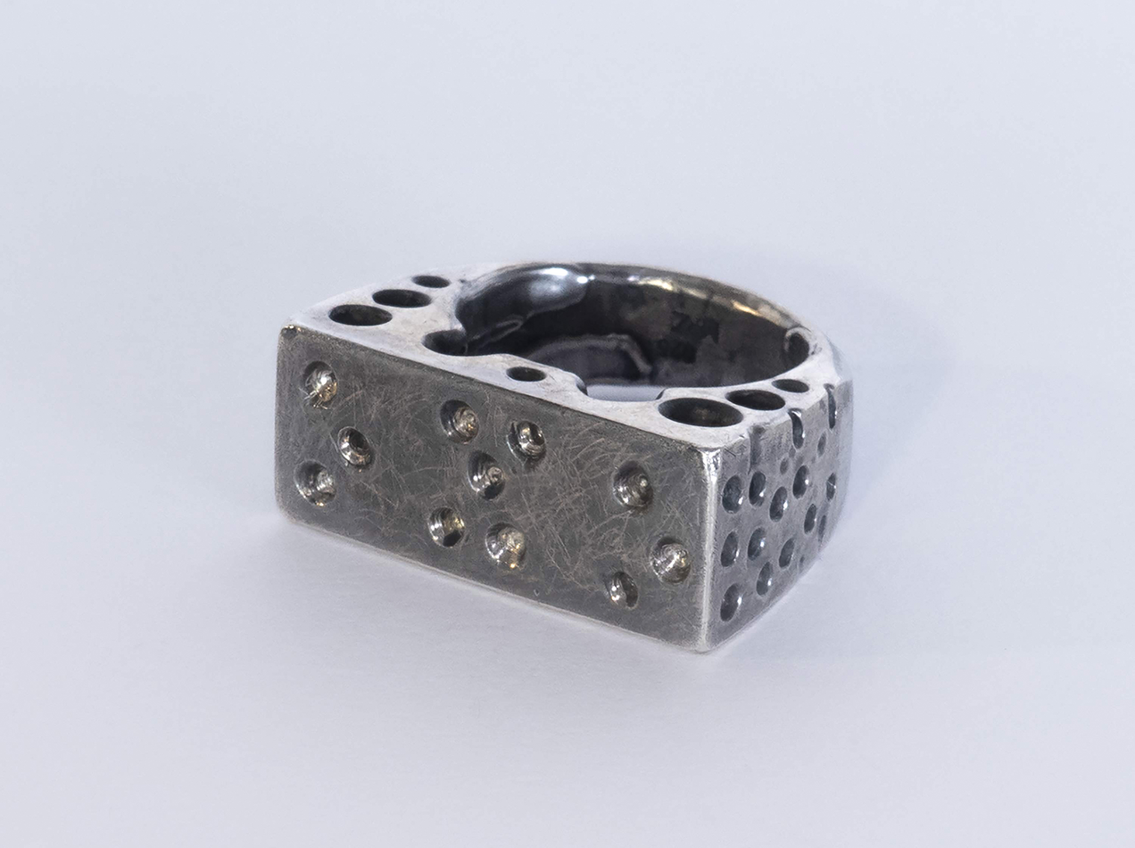"Tunnel" Silver ring showing dimples in braille on the upper surface, the other parts of the ring are perforated