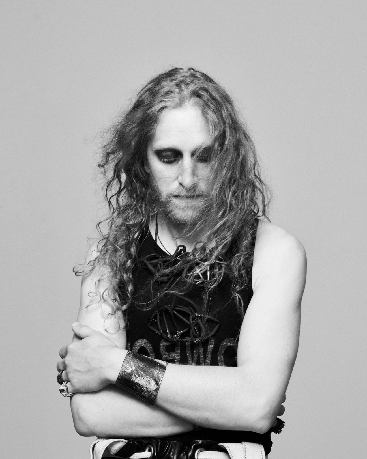 Artist Georg Petermichl wears bracelets, rings and necklaces by Ela Nord over a black tank top, he crosses his arms in front of his chest, his face is serious