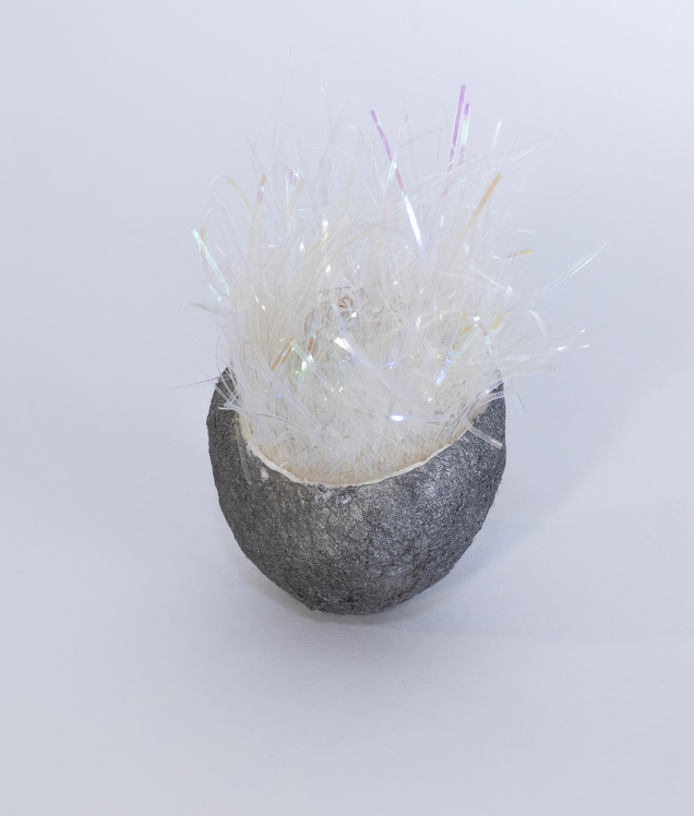 Pendant made of an open dark grey silk cocoon with a kind of shiny fluffy fur oozing out of its inside